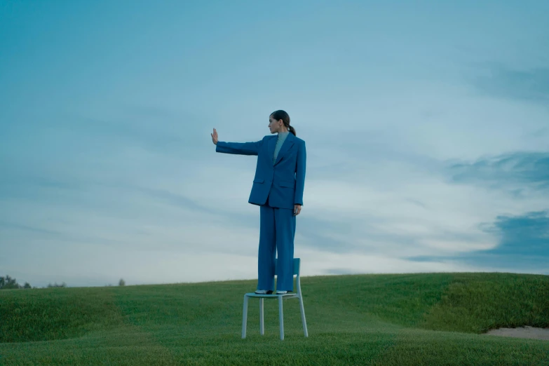 a man in a blue suit standing on a chair, unsplash, surrealism, waving, standing in a grassy field, shin min jeong, billboard image