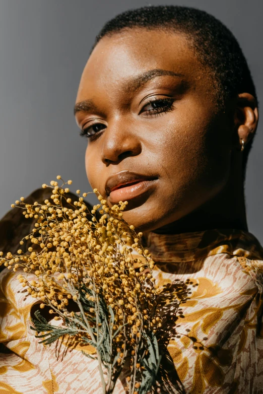 a woman holding a bunch of flowers in front of her face, an album cover, trending on unsplash, brown skin. light makeup, seeds, close - up studio photo, with yellow cloths