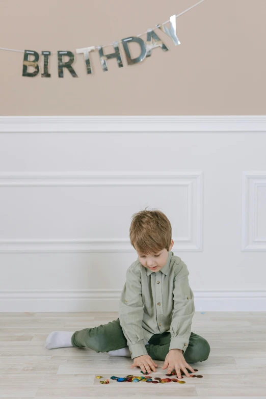 a little boy sitting on the floor in front of a birthday banner, pexels, muted green, leaning against the wall, 1 5 0 4, digital oth
