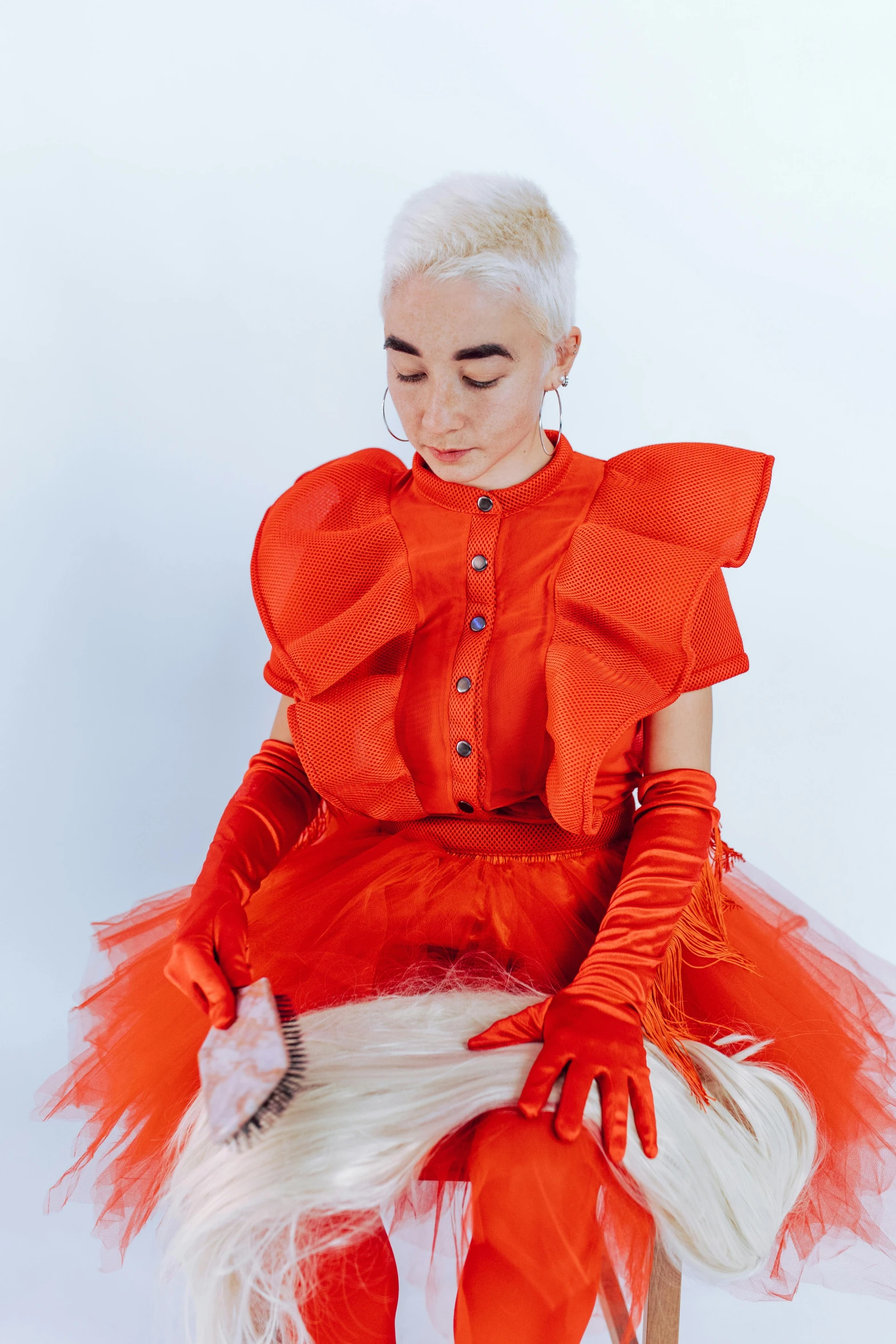 a woman in a red dress sitting on a stool, an album cover, inspired by Marie-Gabrielle Capet, fluffy orange skin, rei kawakubo artwork, an epic non - binary model, red gloves