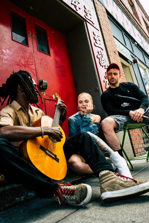 a group of people sitting next to each other on a sidewalk, an album cover, pexels contest winner, antipodeans, shaved head, afropunk, holding a guitar, yzy gap