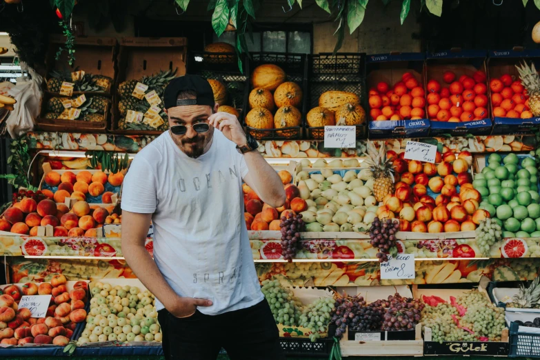 a man standing in front of a fruit stand, an album cover, pexels contest winner, wearing sunglasses and a cap, profile image, enes dirig, sassy pose