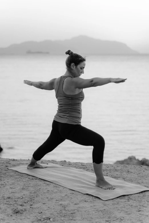 a woman standing on a yoga mat in front of a body of water, a black and white photo, combat stance, warm glow, artemis, clover