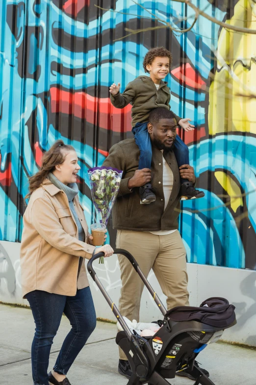 a man and woman walking down a sidewalk with a baby in a stroller, wearing a hoodie and flowers, man walking through city, smiles, family framed on the wall