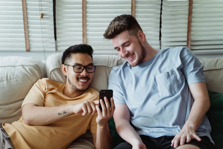 a couple of men sitting on top of a couch, trending on pexels, holds a smart phone in one hand, flirting smiling, avatar image, te pae