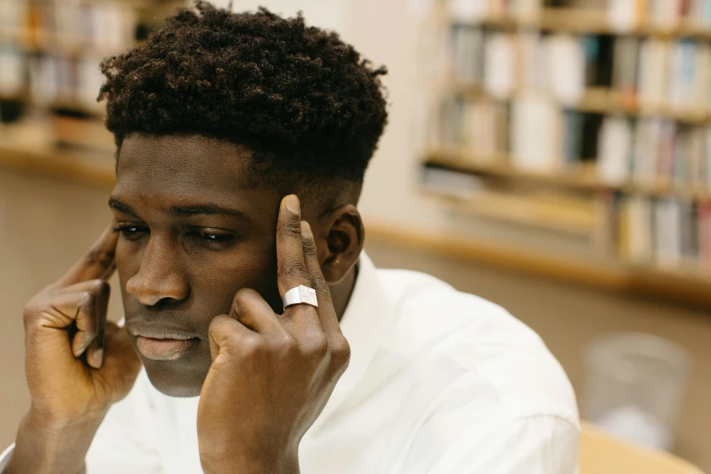 a man talking on a cell phone in a library, by Stokely Webster, trending on pexels, academic art, black teenage boy, looking melancholy, sitting on a mocha-colored table, close - up portrait shot