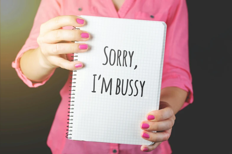 a woman holding a notebook that says sorry, i'm busy, by Julia Pishtar, pixabay, private press, ((pink)), glossy surface, handcrafted, well - dressed