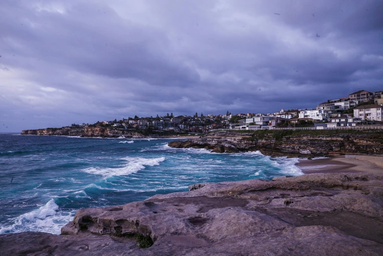 a large body of water next to a beach, a matte painting, pexels contest winner, bondi beach in the background, dark purple clouds, cliffside town, cold stormy wind
