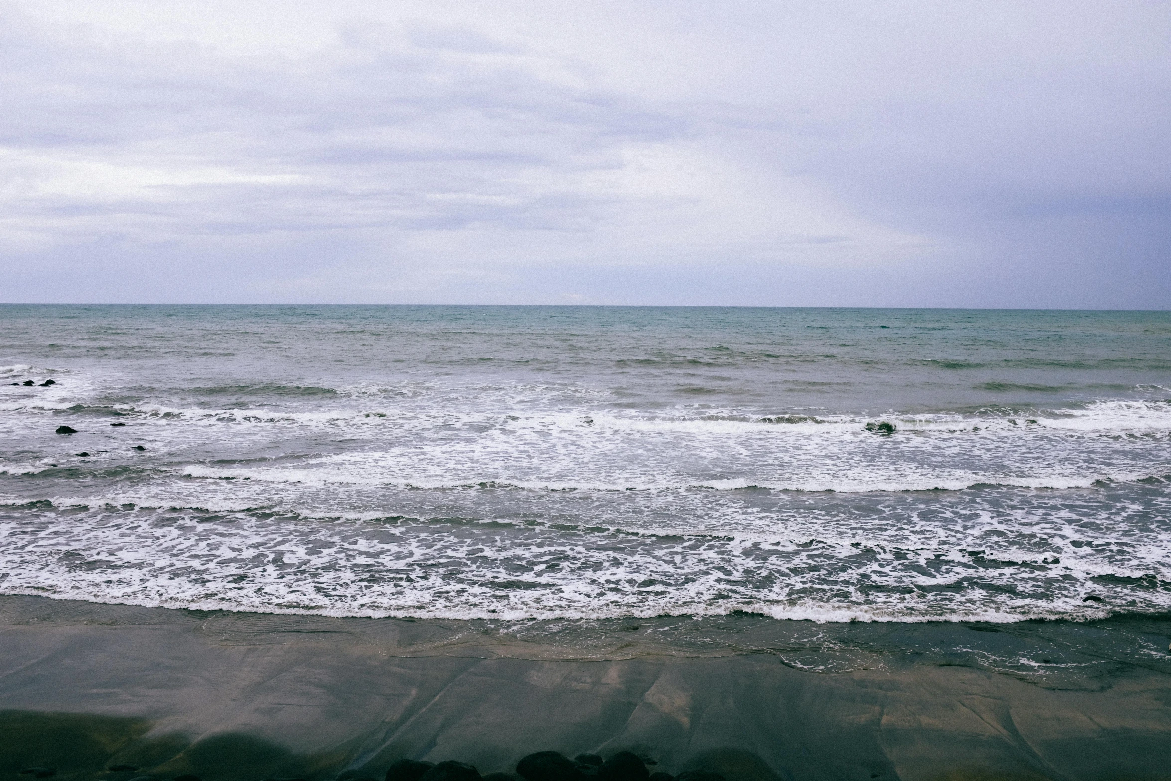 a man riding a surfboard on top of a sandy beach, inspired by Andreas Gursky, unsplash, minimalism, overcast gray skies, japan shonan enoshima, photo of the middle of the ocean, view of sea