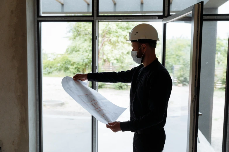 a man standing in front of a window holding a blueprint, profile image, civil engineer, thumbnail, wearing facemask