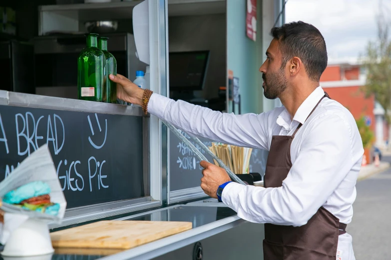 a man standing in front of a food truck, les nabis, hands on counter, holding a bottle, profile image, serving suggestion