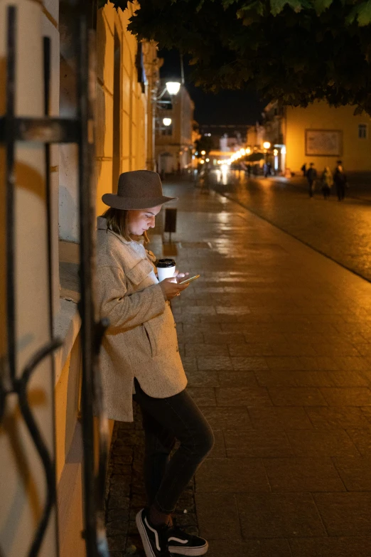 a person standing on a sidewalk using a cell phone, straw hat and overcoat, lights, peruvian looking, square