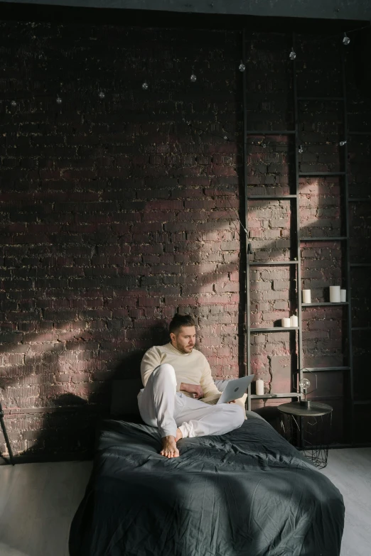 a man sitting on a bed with a laptop, inspired by Elsa Bleda, trending on pexels, renaissance, brick walls, reading nook, wide full body, gray men