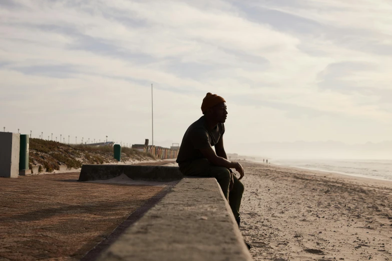 a person sitting on a bench on the beach, by Eglon van der Neer, unsplash, african man, documentary footage, portrait image