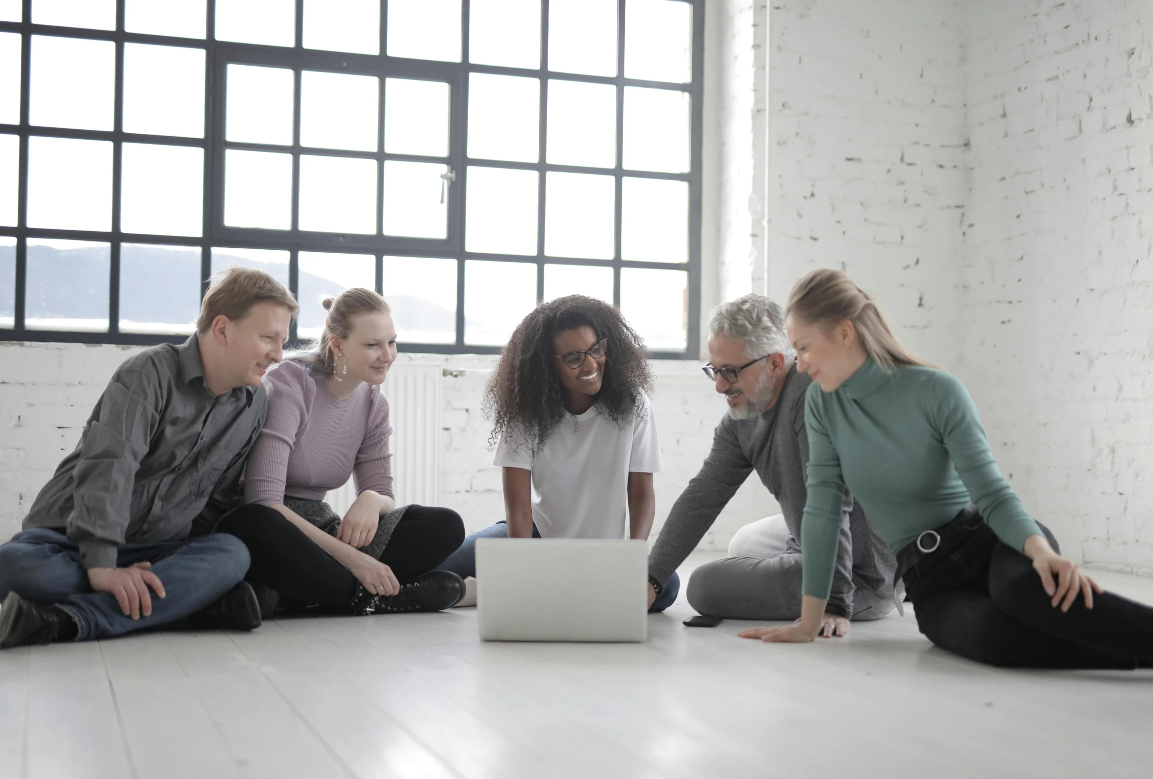 a group of people sitting on the floor looking at a laptop, leaders, grey, coloured, supportive