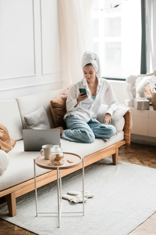 a woman sitting on a couch using a cell phone, tech robes, wearing white pajamas, computer aesthetic, topknot