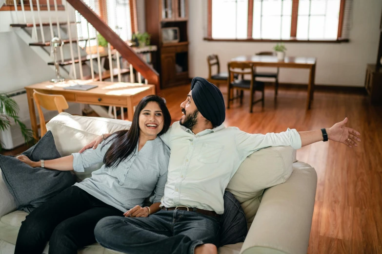 a man and woman sitting on a couch in a living room, inspired by Manjit Bawa, hurufiyya, looking happy, premium quality, guide, profile image