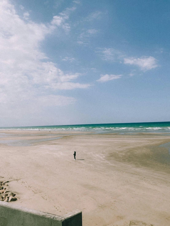 a man standing on top of a sandy beach next to the ocean, image from afar, normandy, instagram post, vsco