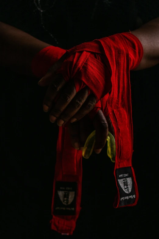 a close up of a person holding a red belt, by Adam Marczyński, bandage taped fists, on black background, uganda knuckles, cloth wraps