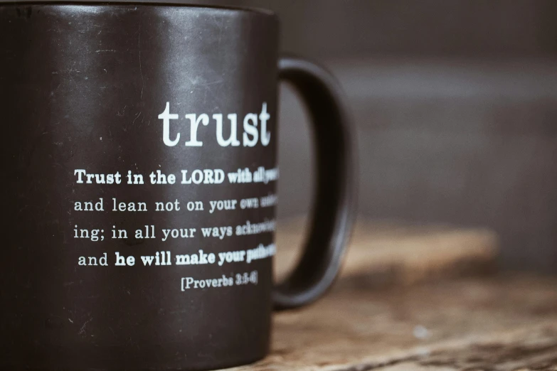 a black coffee mug sitting on top of a wooden table, a picture, by Robbie Trevino, old testament, truth, rust, triumph