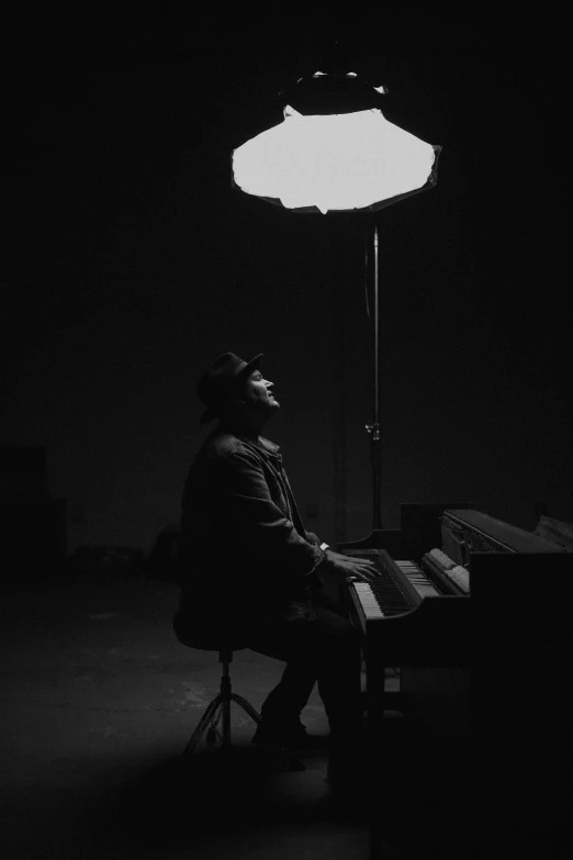 a man sitting at a piano in a dark room, a black and white photo, inspired by Michael Ray Charles, unsplash, conceptual art, he is wearing a hat, sun down, floating alone, on a pale background