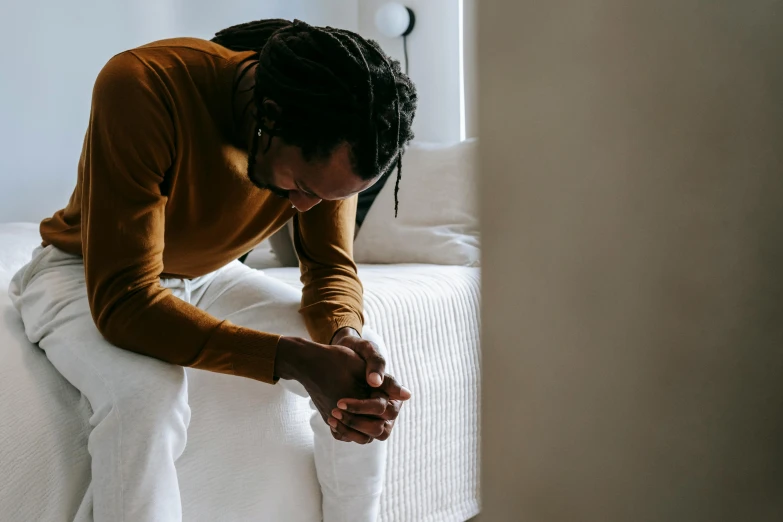 a man sitting on a bed with his hands on his knees, by Nina Hamnett, pexels contest winner, with brown skin, from the elbow, recovering from pain, instagram post