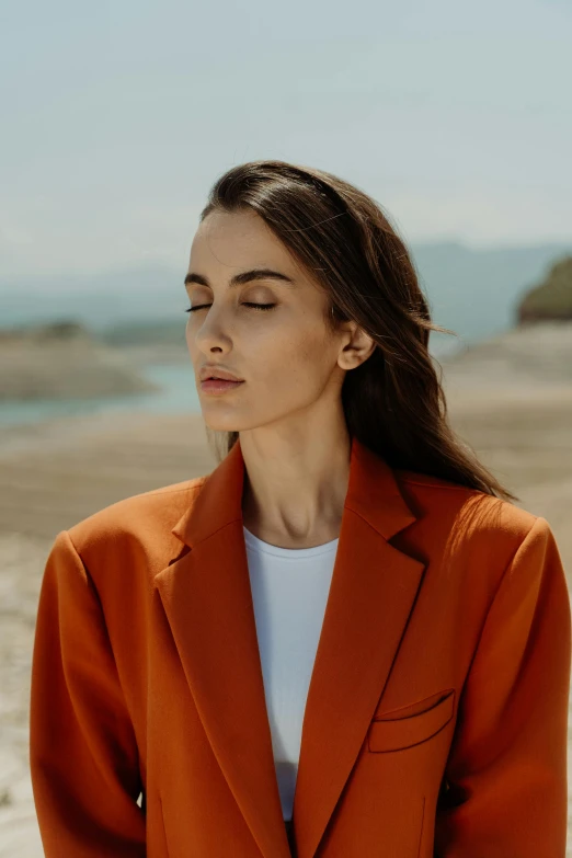 a woman standing on a beach wearing an orange blazer, trending on pexels, slicked-back hair, a mountain look like a women, photoshoot for skincare brand, coral brown hair