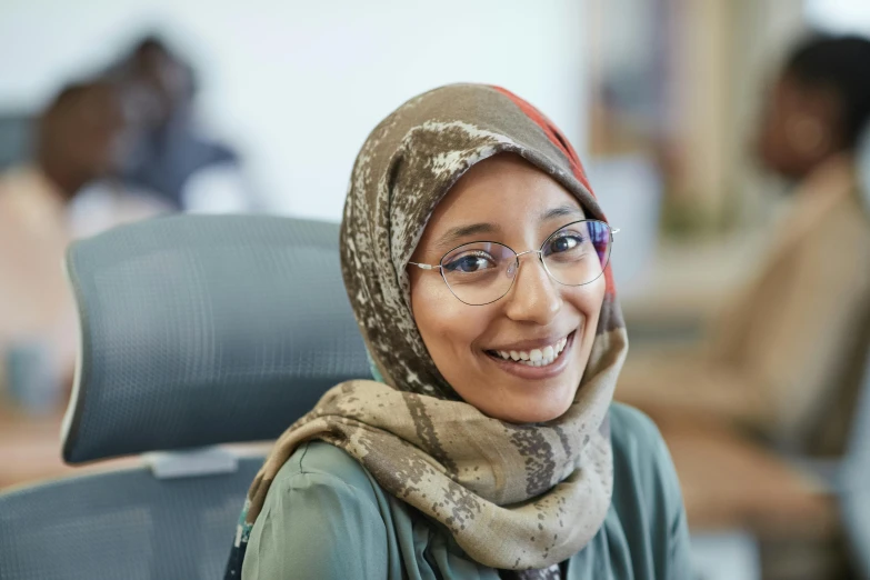 a woman in a headscarf smiles at the camera, hurufiyya, sitting at desk, profile image, with glasses on, multiple stories