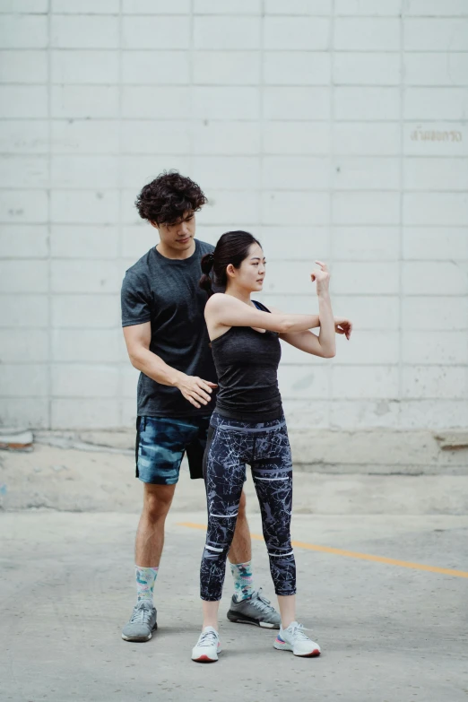 a man and a woman standing in a parking lot, dynamic stretching, lee griggs and jason chan, showing her shoulder from back, square