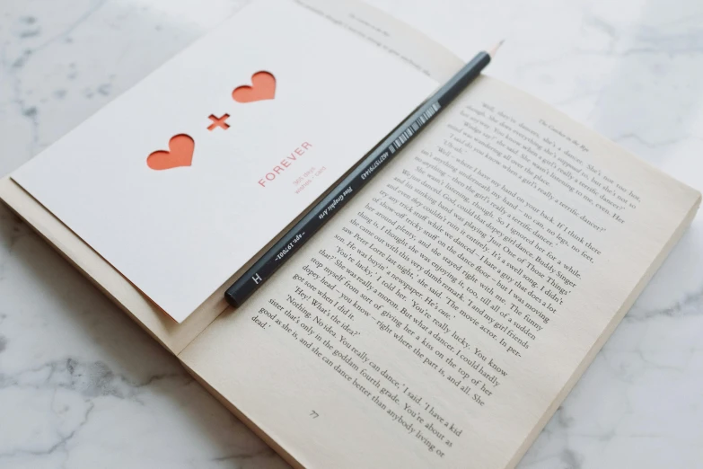 a pen sitting on top of an open book, by Emma Andijewska, pexels contest winner, romanticism, heart - shaped face, readable font, two characters, on white paper