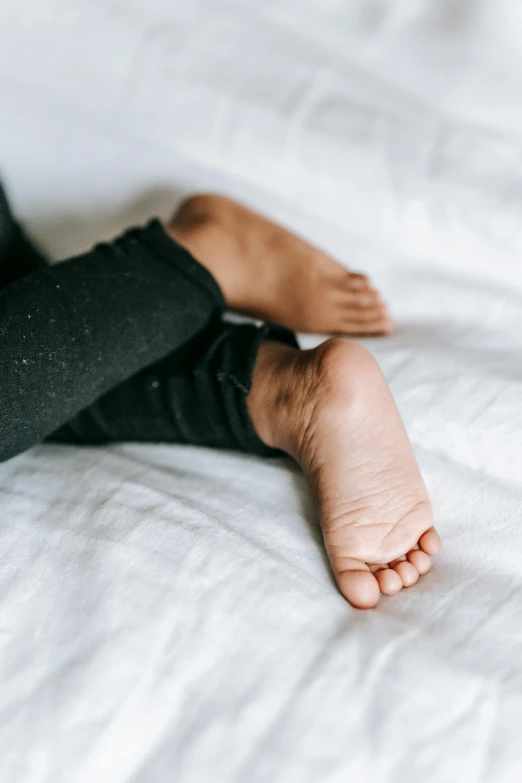 a close up of a person's feet on a bed, young child, smooth textured skin, black textured, barefoot