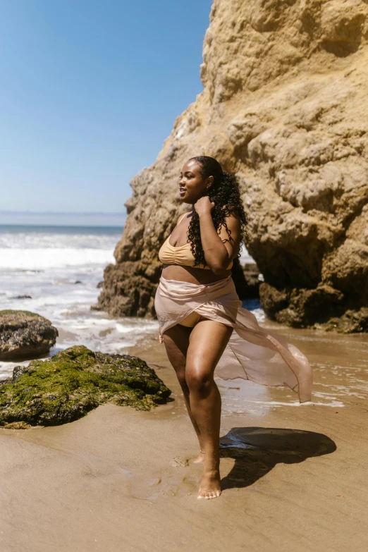 a woman walking on a beach next to the ocean, by Dulah Marie Evans, renaissance, curvy model, slide show, shaquille o'neil pregnant, girl walking in a canyon