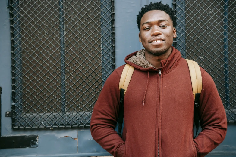 a man with a backpack standing in front of a building, brown skin, background image, red hoodie, thumbnail