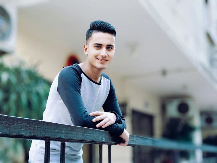 a man leaning on a railing in front of a building, young cute face, ahmad merheb, profile image