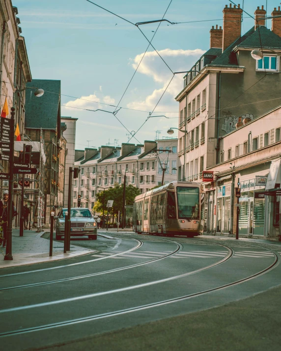 a train traveling down a city street next to tall buildings, by Raphaël Collin, pexels contest winner, art nouveau, rennes - le - chateau, taupe, lgbtq, detmold