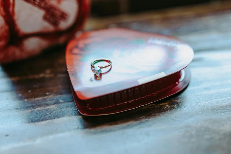 a wedding ring sitting on top of a heart shaped box, an album cover, by Julia Pishtar, pexels contest winner, tin can, red emerald, miniature product photo, metal lid