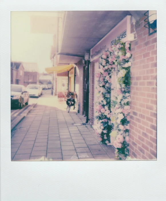 a building with a bunch of flowers on the side of it, a polaroid photo, unsplash, stood outside a corner shop, flash polaroid photo, pale colors, 7 0 mm photo