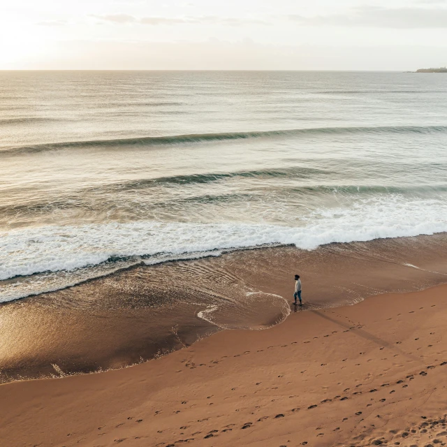 a couple of people standing on top of a sandy beach, pexels contest winner, lone person in the distance, surfing, early morning lighting, red sand beach