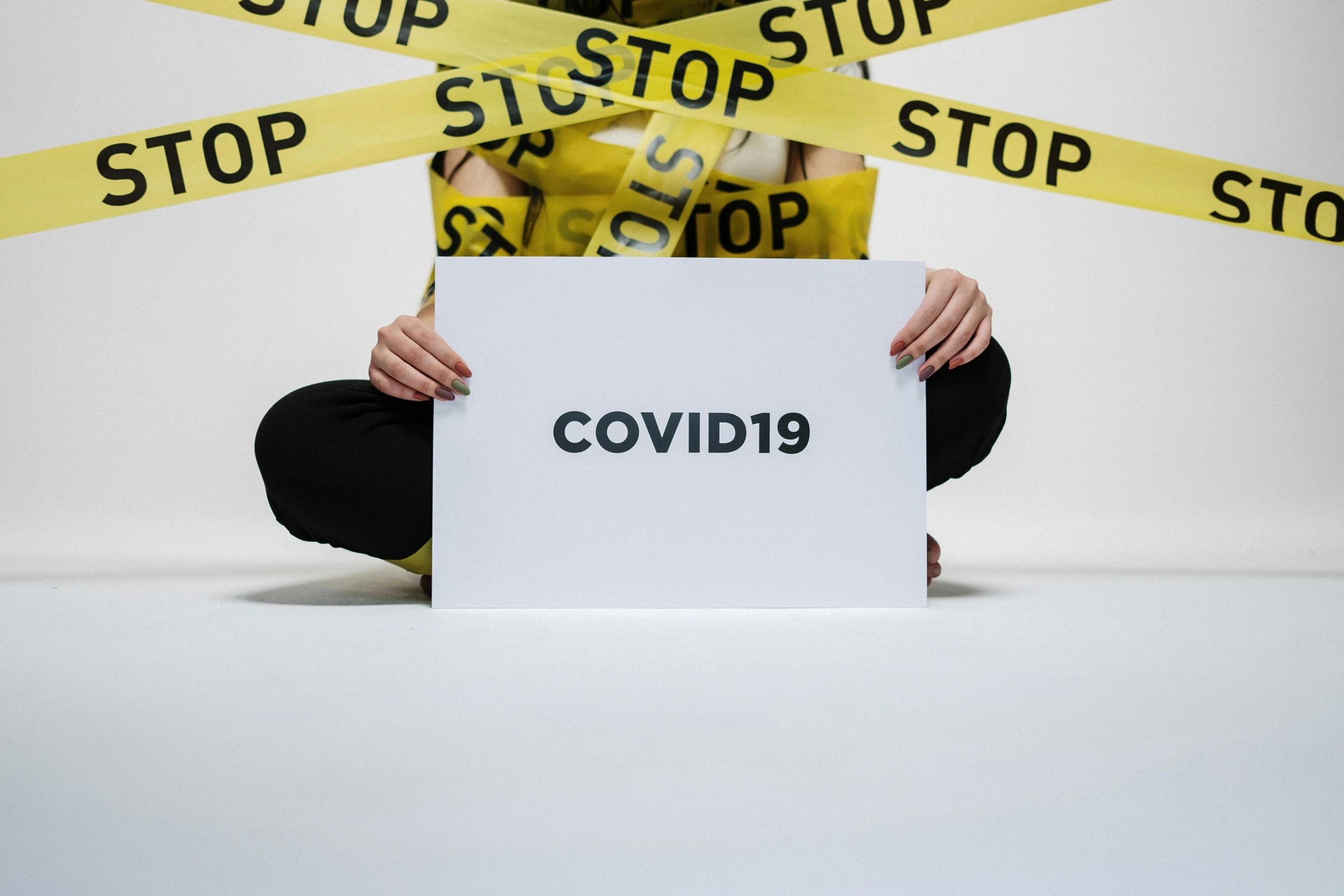 a woman sitting on the floor holding a sign, by Olivia Peguero, trending on pexels, cute coronavirus creatures, police tape, cover corp, a person standing in front of a