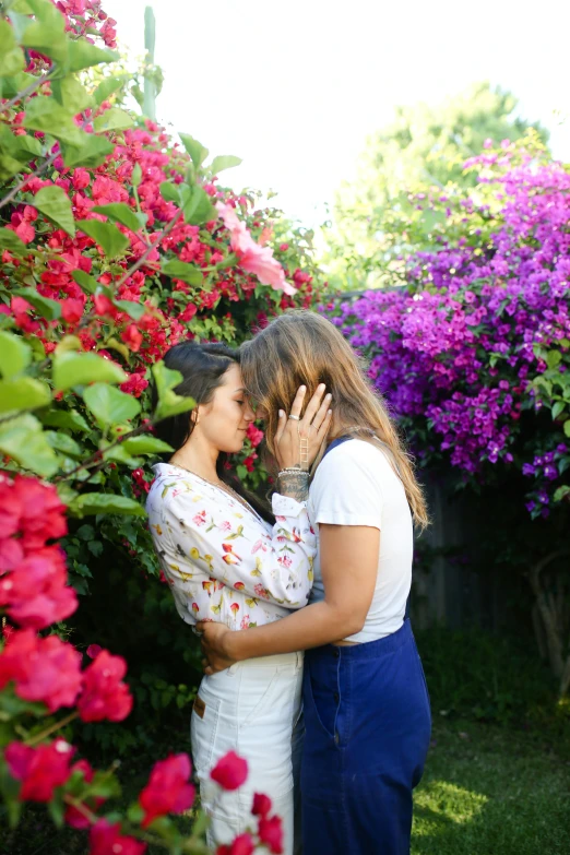 a couple of women standing next to each other in a garden, unsplash, romanticism, bougainvillea, lesbian embrace, brunette, jen atkin