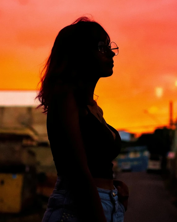 a woman standing in the middle of a street at sunset, a picture, trending on pexels, queer woman, girl with glasses, profile image, black teenage girl