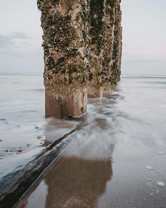 a large rock sitting on top of a beach next to the ocean, pillars, in the evening, in a row, rivulets