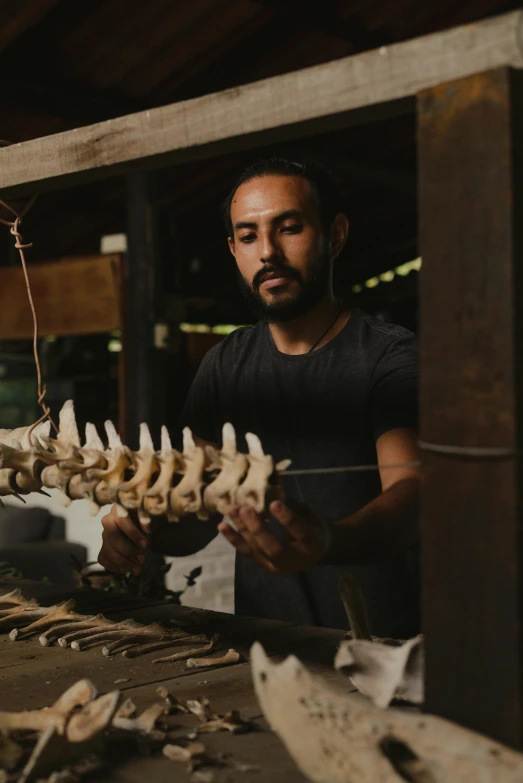 a man standing in front of a bunch of bones, by Jessie Algie, pexels contest winner, kinetic art, in a workshop, half shark alligator half man, profile image, thiago alcantara