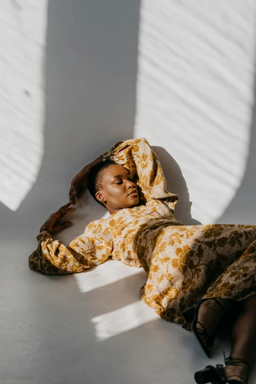 a woman laying on top of a white floor, by Nina Hamnett, trending on unsplash, light and space, wearing an african dress, in a gold suit, wearing a robe, low sun