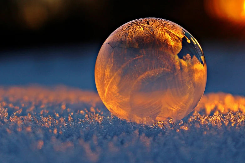 a glass ball sitting on top of a snow covered ground, during a sunset