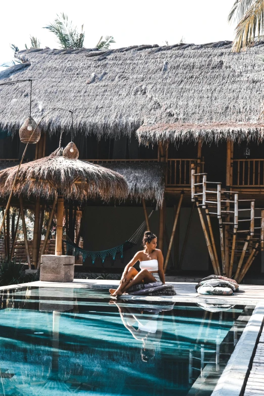 a woman sitting on the edge of a swimming pool, trending on unsplash, bamboo huts, village, full sun, textured