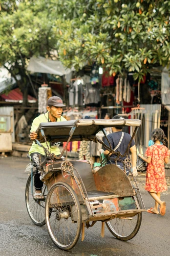 a man riding on the back of a bike down a street, ancient indonesia, square, photo taken in 2 0 2 0, carriage
