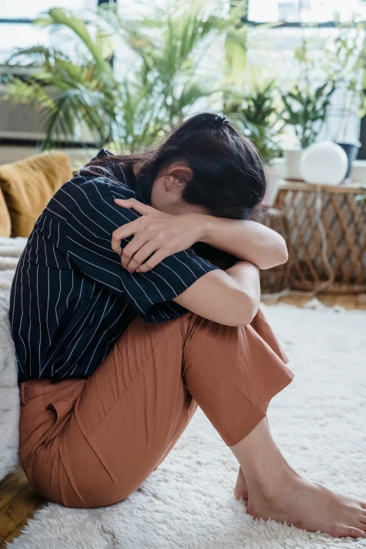 a woman sitting on the floor with her head in her hands, trending on pexels, crying and reaching with her arm, sitting on a couch, hunched shoulders, asian woman