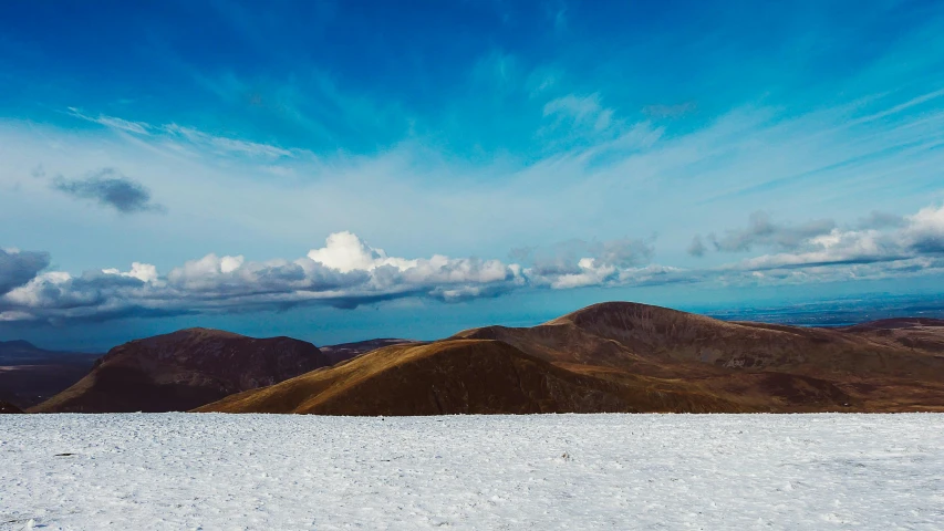 a person standing on top of a snow covered slope, by Peter Churcher, unsplash contest winner, minimalism, irish mountains background, blue sky and white clouds, there is a place in wales, the panorama