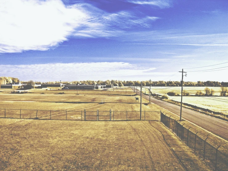 a field with a fence in the middle of it, a tilt shift photo, by Carey Morris, unsplash, land art, roswell air base, clear blue sky vintage style, parking lot, with instagram filters